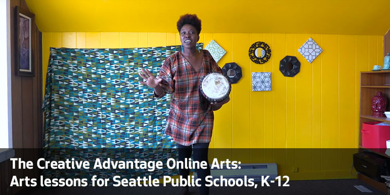 An African teach artist stands with a drum in bright yellow room. The Creative Advantage Online Arts: Arts lessons for Seattle Public Schools, K through 12.